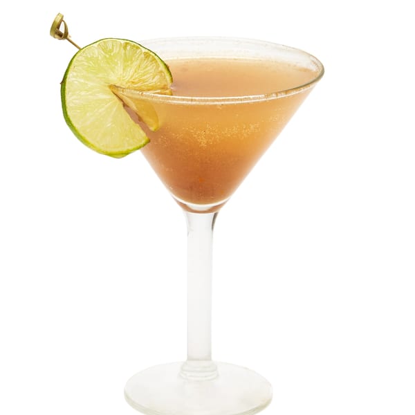 A Muna cocktail in a martini glass, garnished with a lime wedge on a white background.