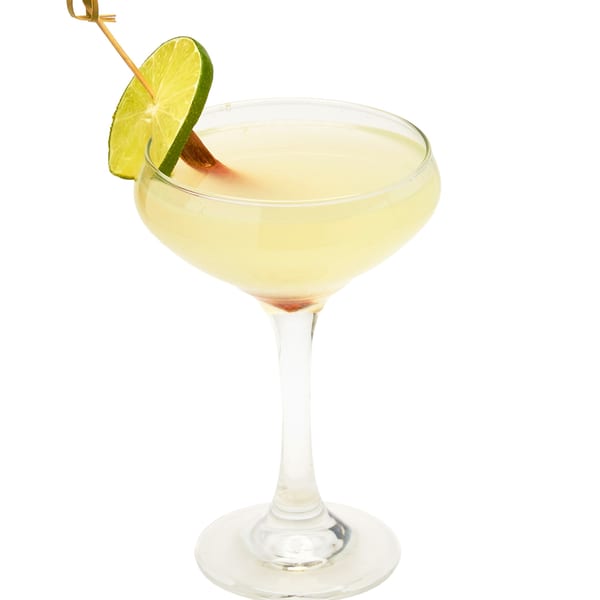 Muna's light yellow cocktail in a coupe glass, garnished with a lime wedge and cinnamon stick.