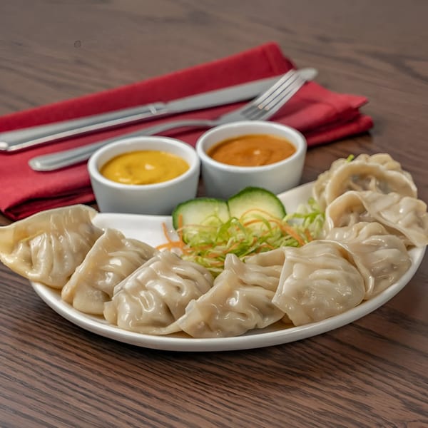 Muna's steamed momos with two dipping sauces, salad, and cutlery on a wooden table.