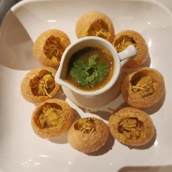 Muna's pani puri, a traditional Indian street food, with a small pitcher of spiced water and seven crispy shells.