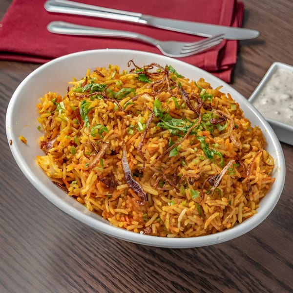 A white bowl of Muna's Indian biryani, garnished with fried onions and fresh herbs.