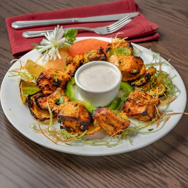 Muna Indian chicken tikka with sauce, lemon, and garnish on a white plate with red napkin.