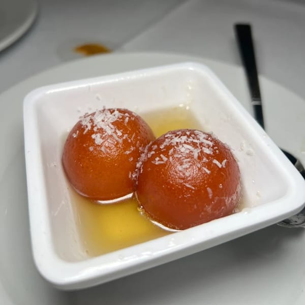 Two gulab jamun, Indian fried dough balls, in syrup, topped with coconut flakes in a white dish.