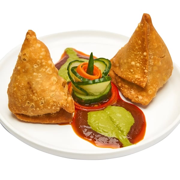 Two golden-brown Muna samosas with green and red chutneys, garnished with cucumber and carrot.
